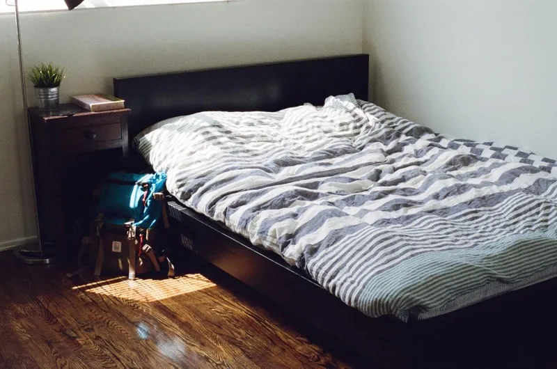 A double bed pushed into the corner of a bedroom, with a nightstand wedged between the headboard and the wall and a narrow strip of floor left along one side.